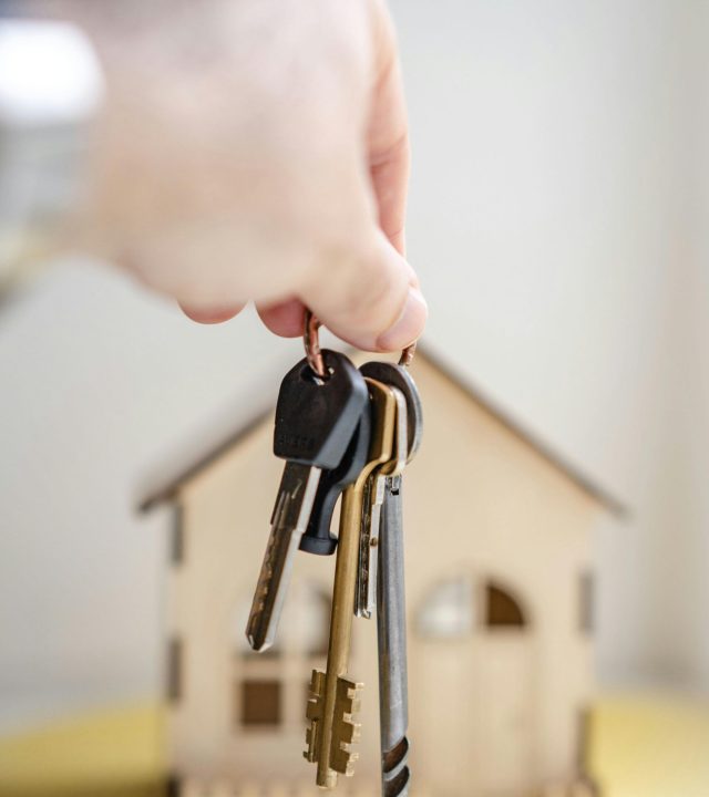 pexels photo 7599735 7599735 Close-up of a hand holding keys with a miniature wooden house in the background, symbolizing real estate investment.